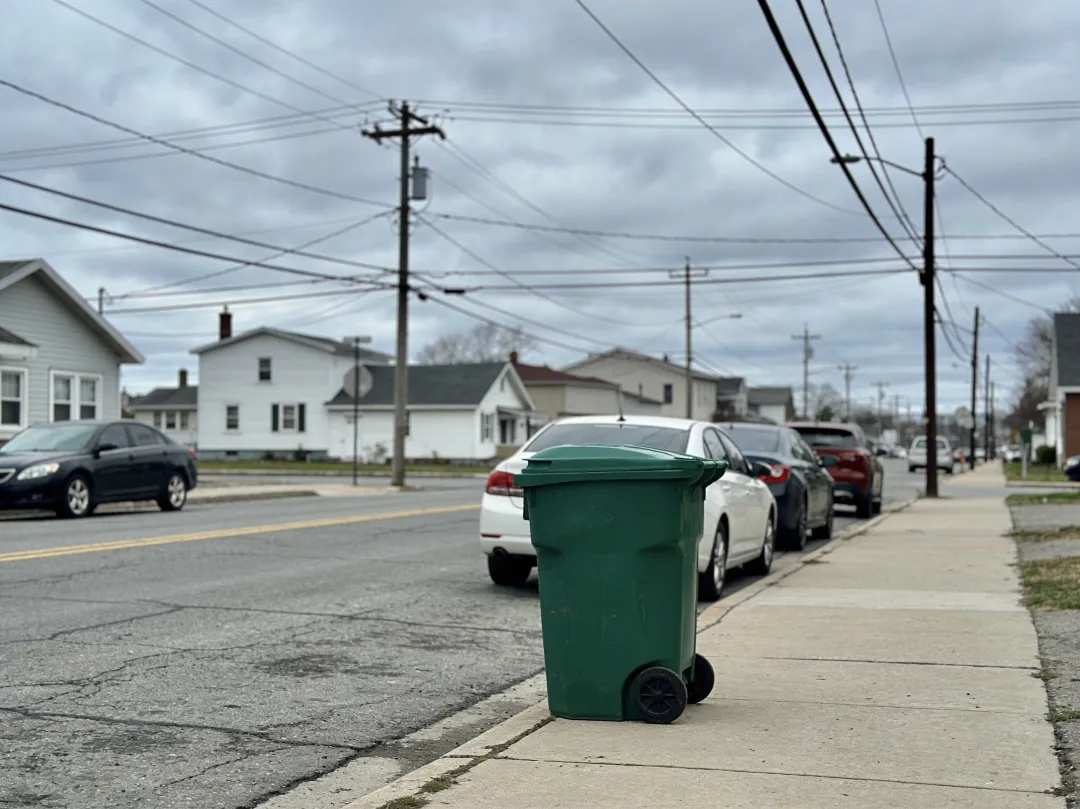 AI photo edit — before: a residential street with overhead power lines crossing the sky and a green trash bin on the sidewalk