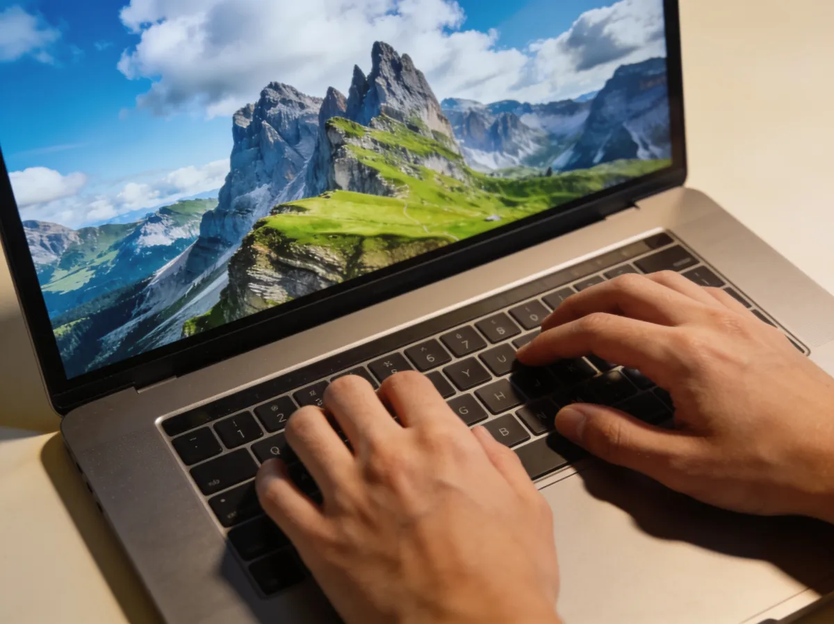 AI-generated image — hands typing a sentence on a laptop as a vivid mountain landscape forms on the screen.