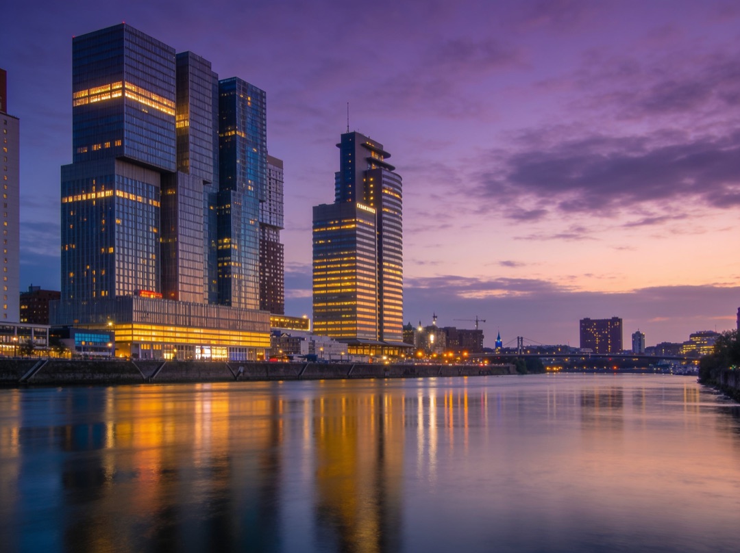 Original photo — riverside city skyline at dusk with lit towers reflected in the water, before AI editing