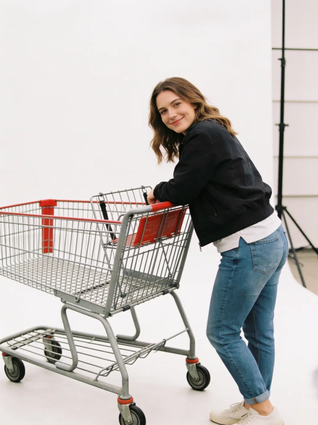 AI photo edit — the same woman and shopping cart in a modern white photo studio with a seamless backdrop and light stand